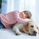 Happy kid  with down syndrome and Labrador retriever cuddling on